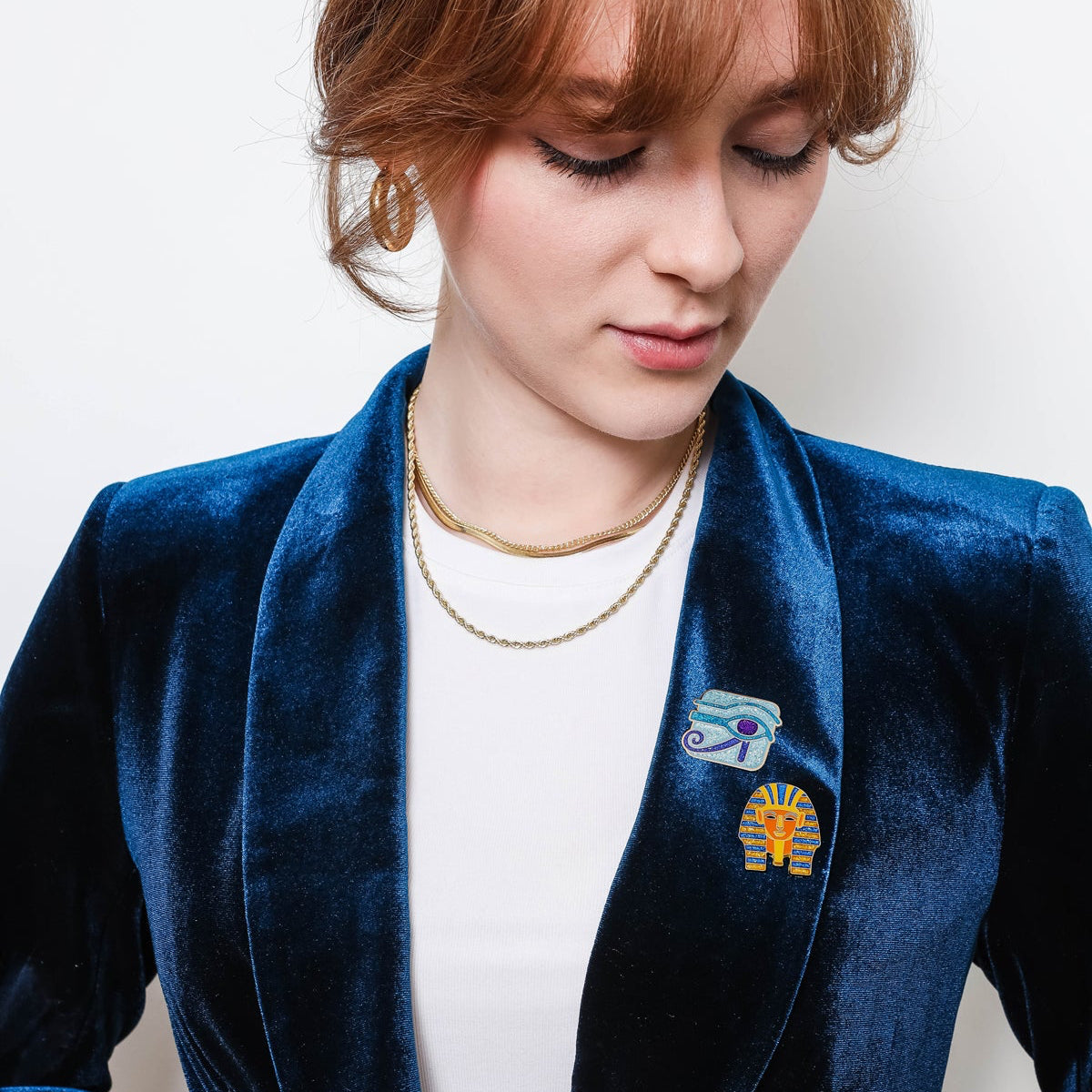 Person wearing a blue blazer with a Eye of Horus & King Tut Enamel Pin badges, against a plain background.