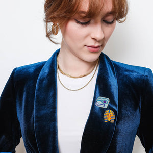 Person wearing a blue blazer with a Eye of Horus & King Tut Enamel Pin badges, against a plain background.
