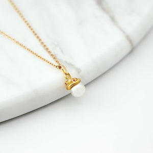 Gold necklace with a pearl pendant on a white surface