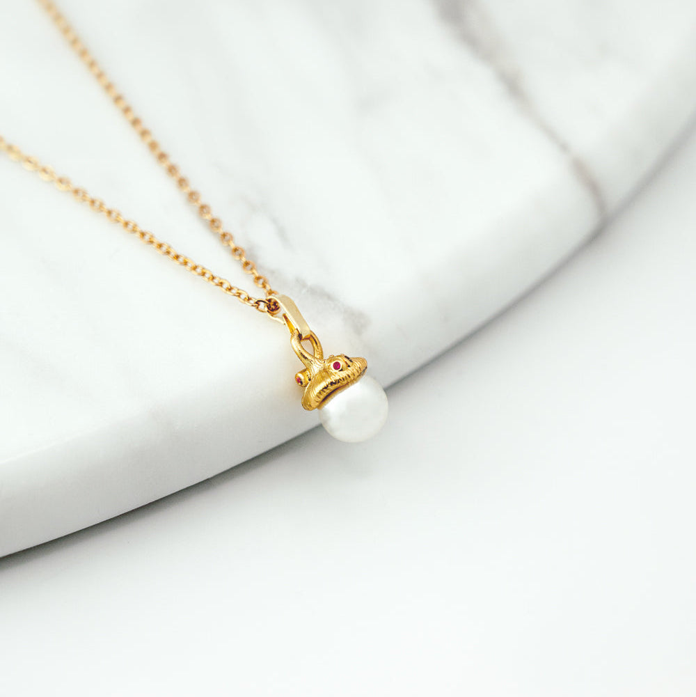 Gold necklace with a pearl pendant on a white surface
