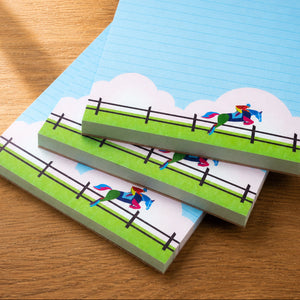 Three lined notepads with a colorful equestrian scene on the cover, stacked on a wooden tabletop.