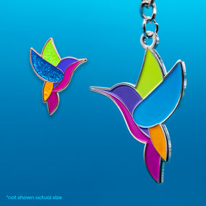 An enamel keychain and pin featuring a colorful hummingbird design against a blue background.