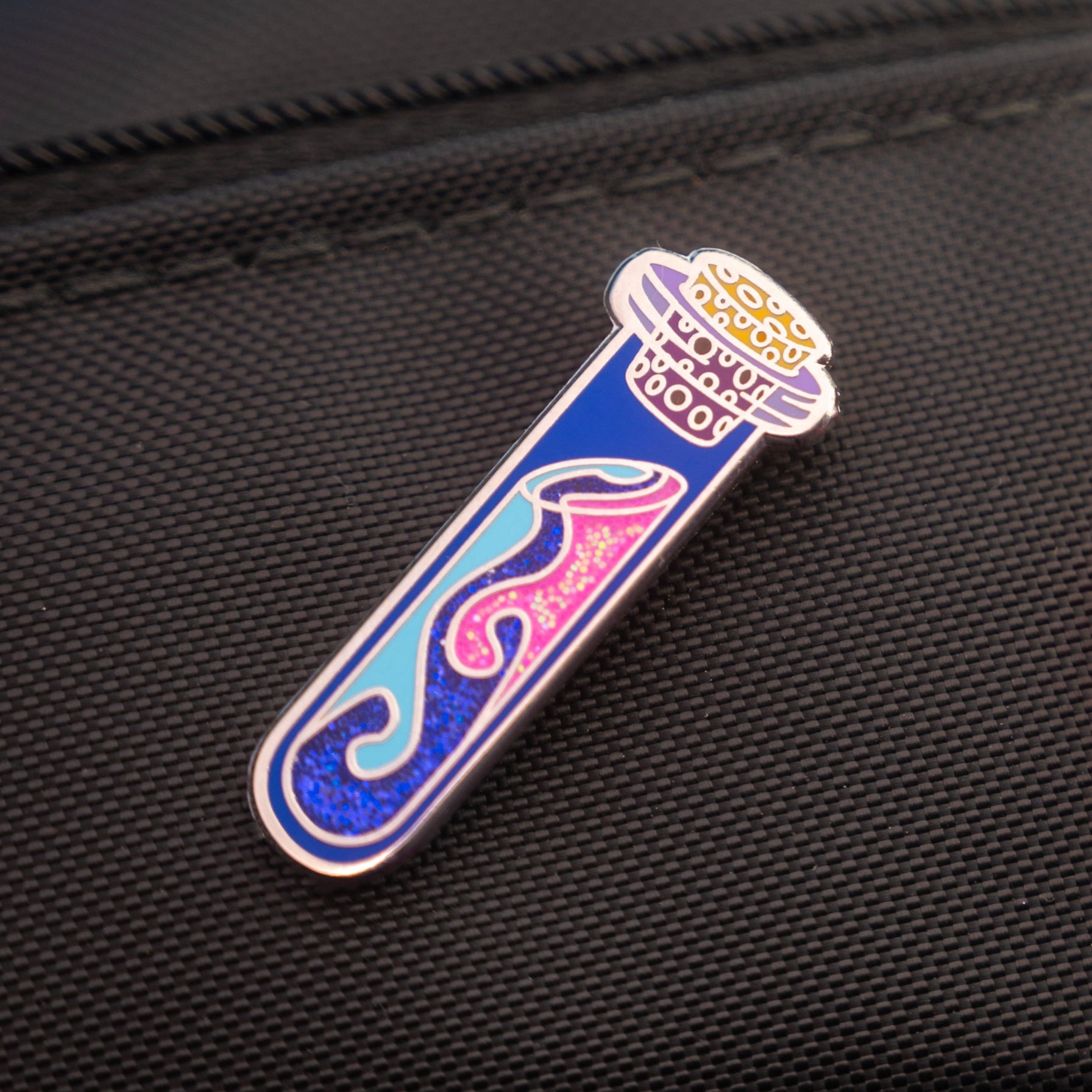 Colorful magic potion vial glittery enamel pin on a black bag.