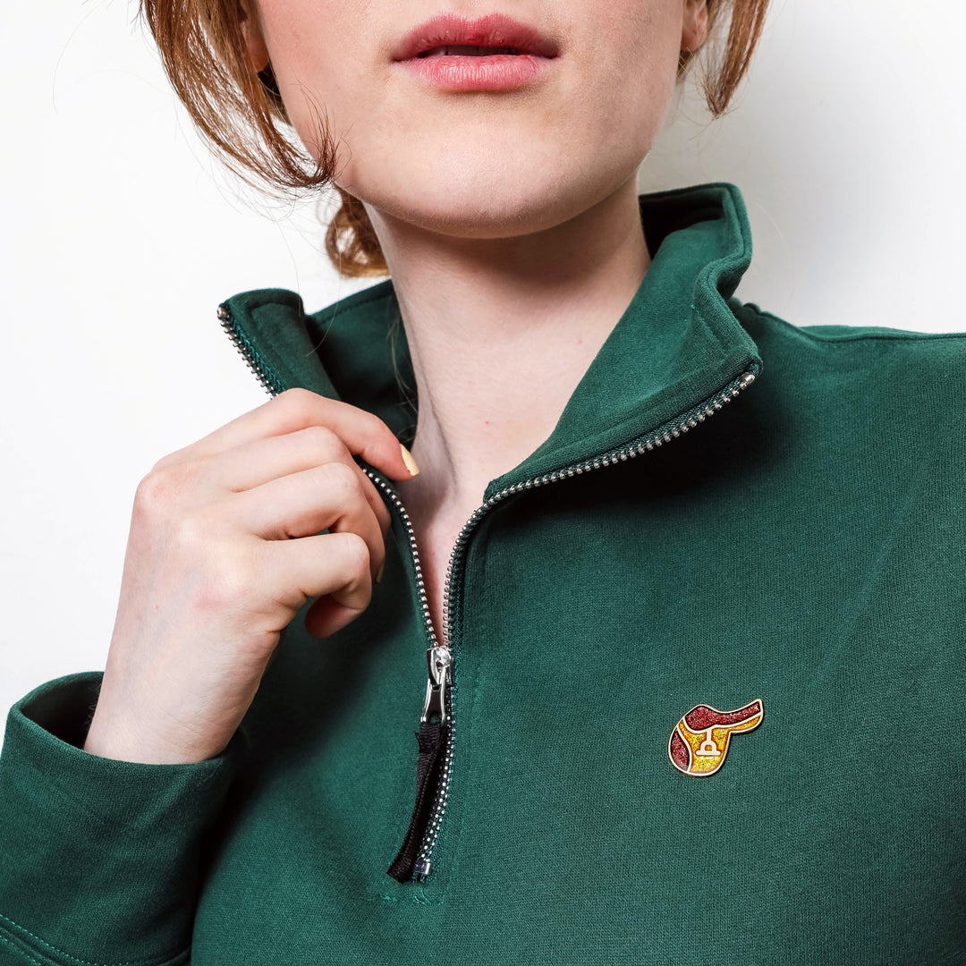 Woman wearing a green fleece pullover with a English Saddle Enamel pin on a white background.