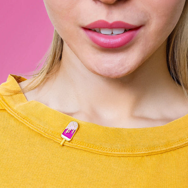Person wearing a pink cream pop enamel pin on a yellow t-shirt against a pink background