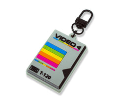 A keyring with a soft PVC rubber sleeve designed to resemble a retro VHS tape with a colorful label.