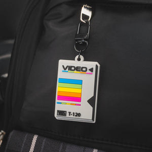 Black backpack with a 'Video' tape cartridge keychain on a blurred background