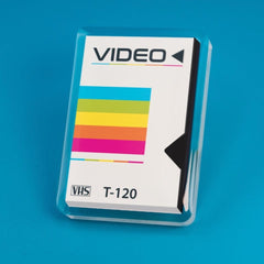 An acrylic pin designed to resemble a retro VHS tape sleeve with a colorful stripe design and the label 'VIDEO VHS T-120' from Spot Studio Art
