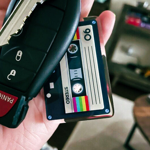 Car key fob with a cassette tape design keychain held in a hand, with a blurred background.