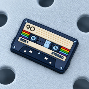 Close-up of the cassette tape charm showing its rainbow stripes, blue reels, cream label, and SIDE 1 and STEREO details.