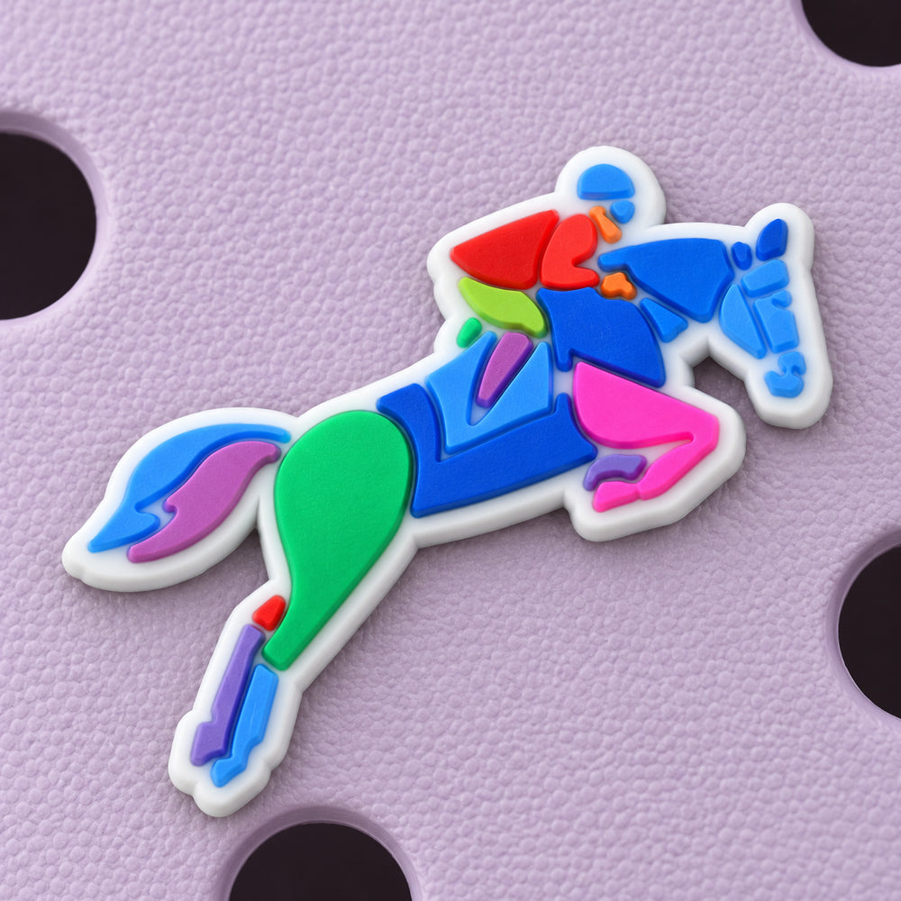 Close-up of the jumping horse and rider charm showing its blue, green, pink, purple, and red raised details and white border.