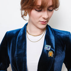Person wearing a blue blazer with a Eye of Horus & King Tut Enamel Pin badges, against a plain background.