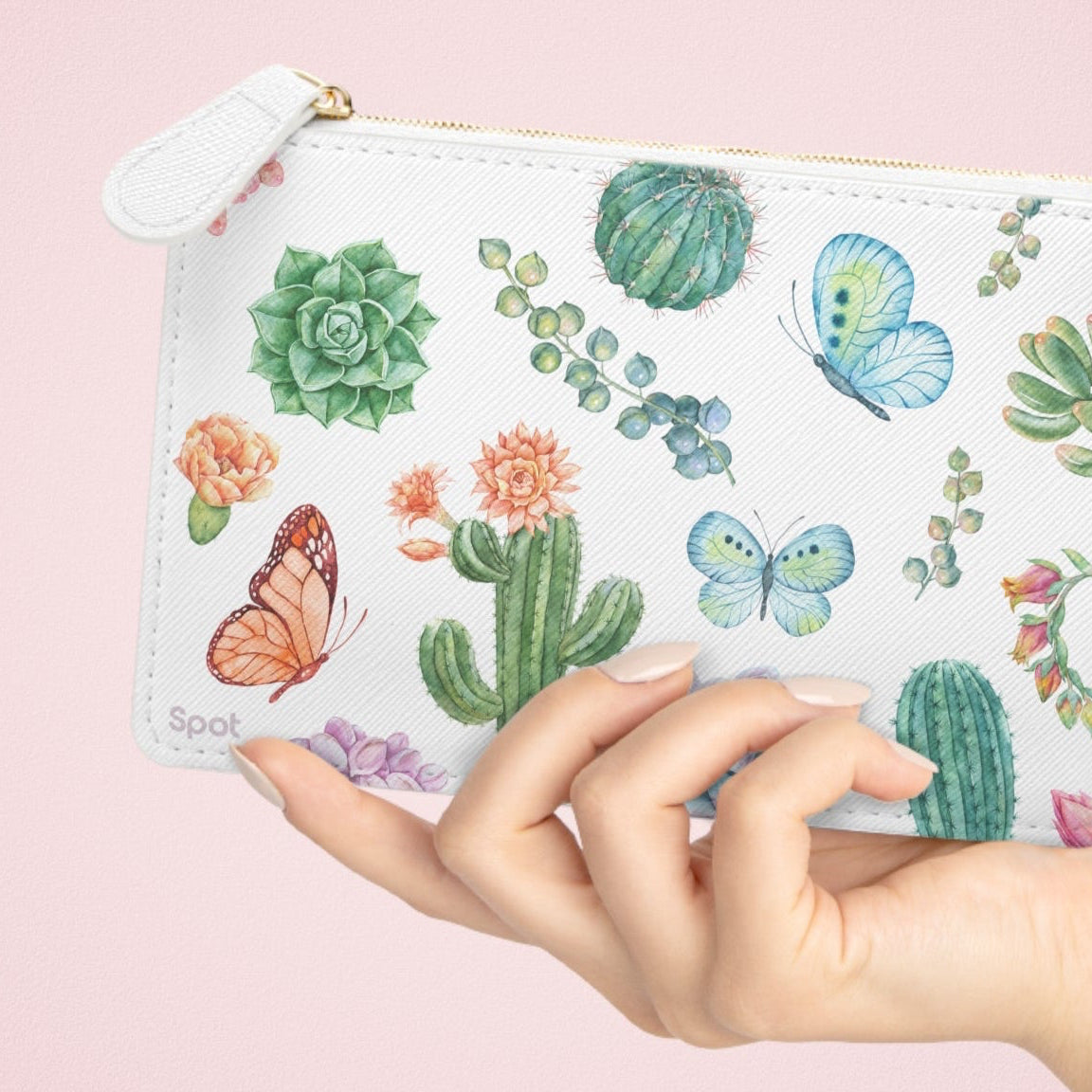 Hand holding a pouch with cactus and butterfly design on a pink background