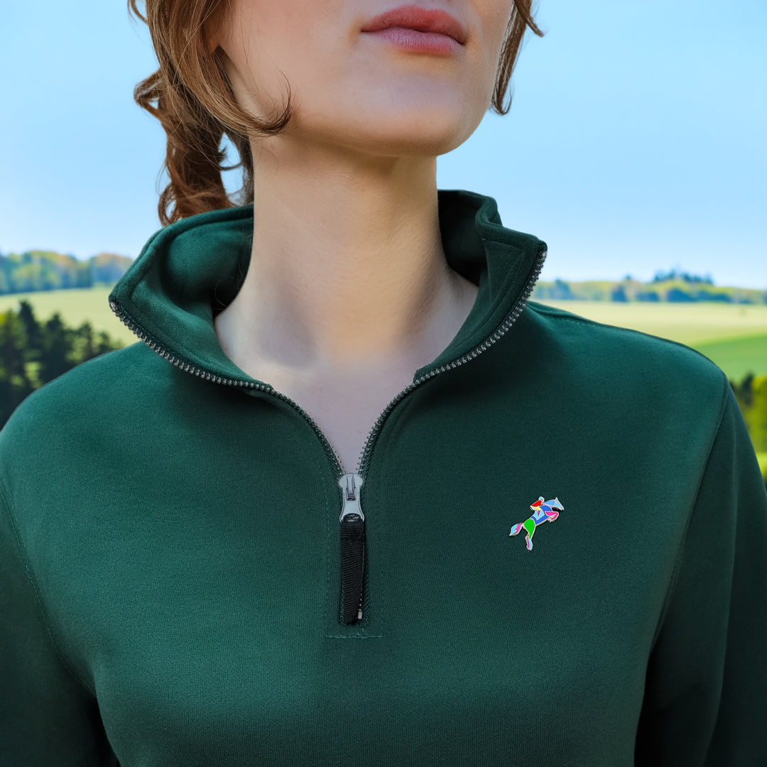 Person wearing a green fleece jacket with a Equestrian Horse Jumping Enamel Pin from Spot Studio Art on a blurred outdoor background.