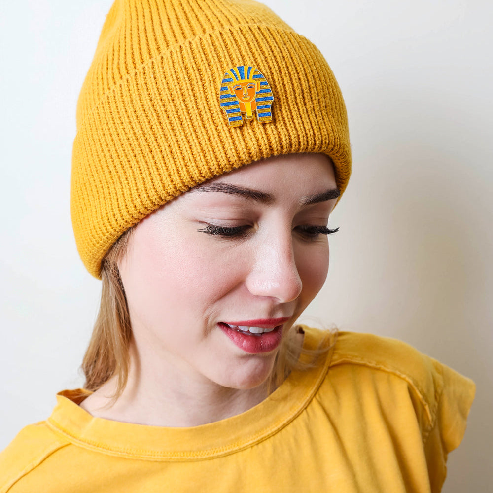 Woman wearing a yellow beanie with a King Tut Enamel Pin on it.