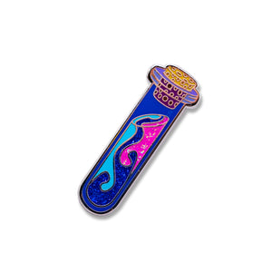 An enamel pin designed as a vial with a blue and pink glitter inlay and silver plating.