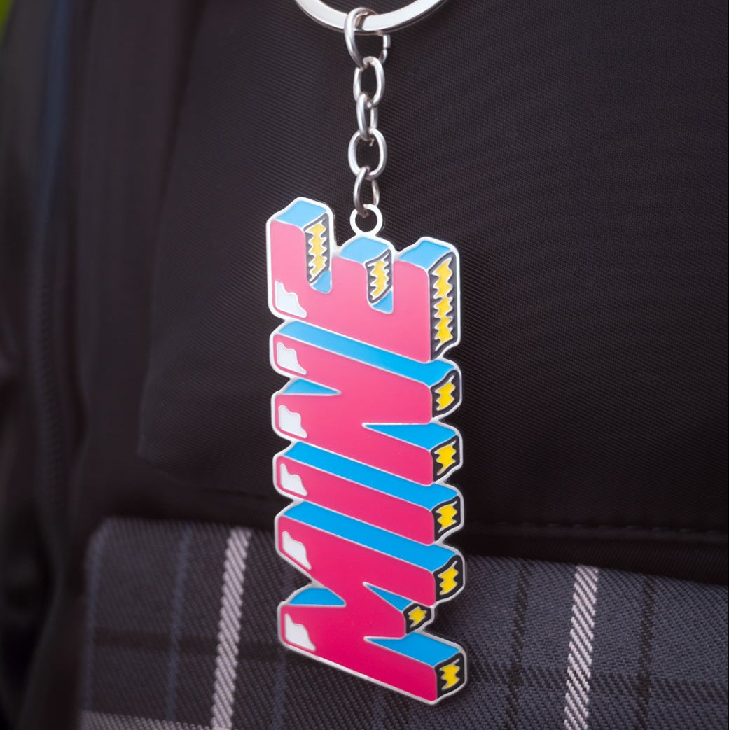 Colorful 'MINE' keychain attached to a black backpack