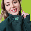 Woman wearing a green jacket with a monstera leaf emblem on a green background
