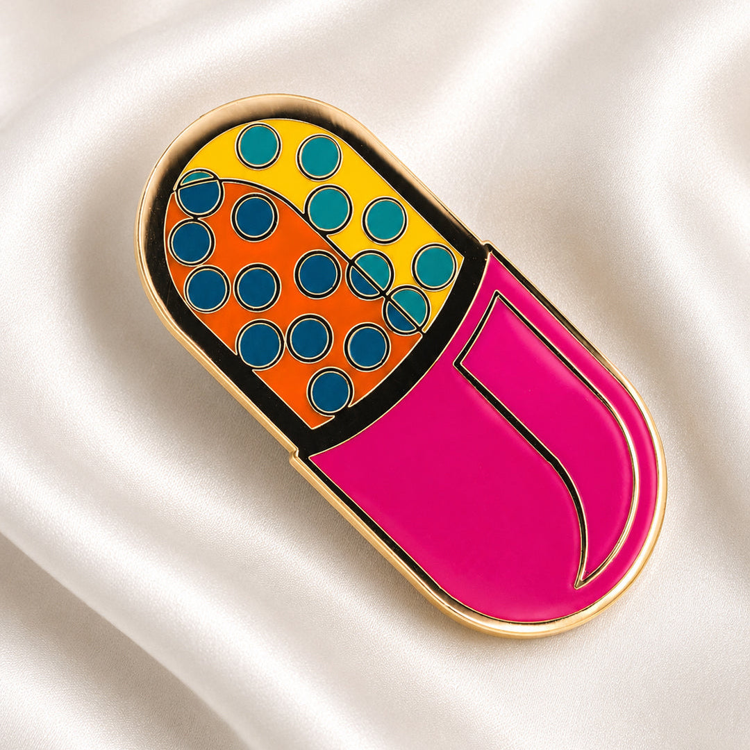 Colorful pill-shaped enamel pin on a satin surface