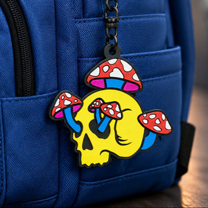Colorful mushroom skull charm attached to a blue backpack on a wooden surface.