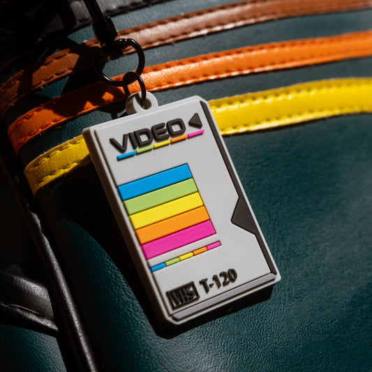 Vintage-style video cassette keychain from Spot Studio art attached to a vintage leather bag.
