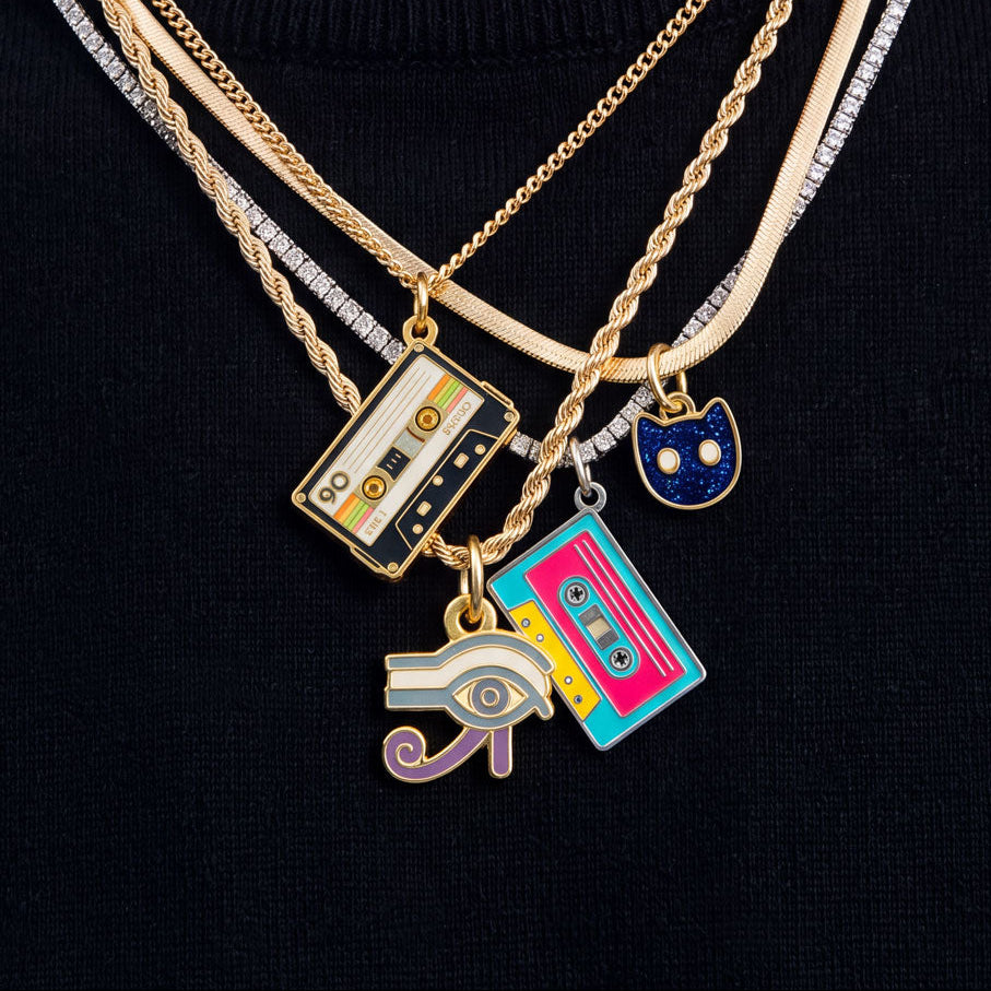 Layered gold and silver necklaces with retro cassette tape and cat-shaped charms, displayed on a black knit top.