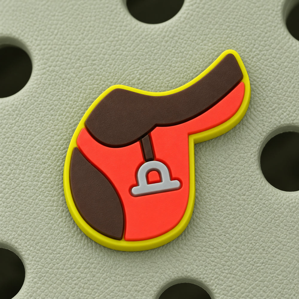 Sharp close-up of the English saddle charm showing its curved brown seat, red flap, yellow-green border, and silver-gray stirrup.