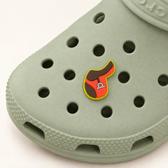 English saddle shoe charm in red and chocolate brown with yellow-green trim and a silver-gray stirrup, mounted on a sage-green Croc.
