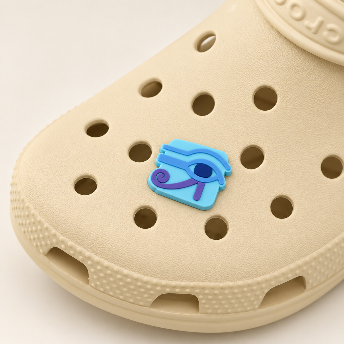 Turquoise Eye of Horus shoe charm with blue and purple details on a buttercream Croc, shown in a three-quarter detail view.