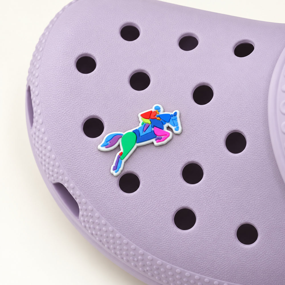Colorful horse-and-rider jumping shoe charm with a white outline attached to a pale lilac Croc, shown in a three-quarter detail view.