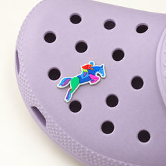 Colorful horse-and-rider jumping shoe charm with a white outline attached to a pale lilac Croc, shown in a three-quarter detail view.